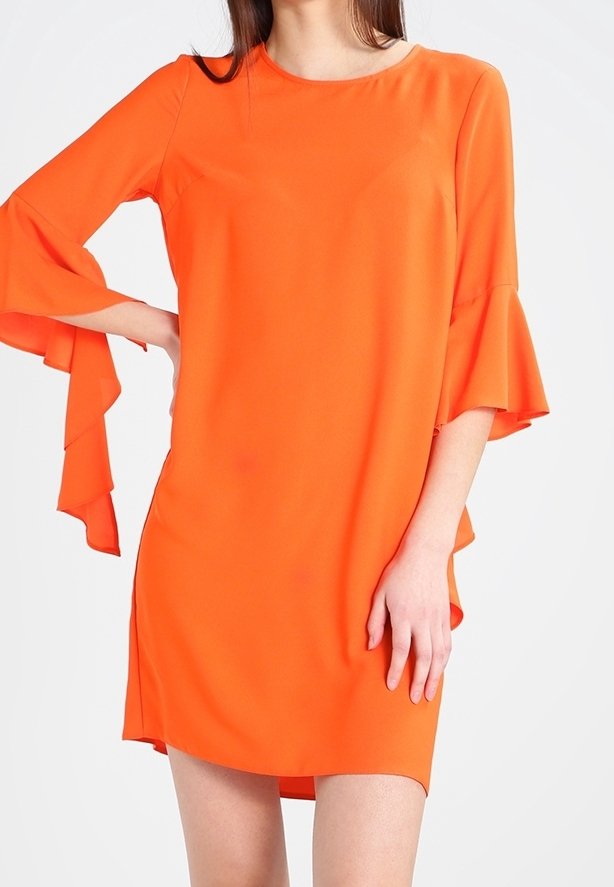 Femme portant une robe orange vif longueur genoux avec des manches trois-quarts évasées et superposées sur un fond blanc uni.