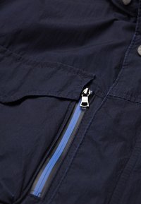 Tissu de veste bleu marine avec une surface texturée, comportant une poche zippée avec des accents bleu et gris et une tirette de fermeture éclair en argent.
