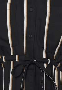 Mustapukuinen nappilukolla varustettu mekko, jossa on pystysuunnassa vaaleita ja ruskeita raidoja. Mekossa on solmittava vyötärö ja kaksi rintataskua. Kankaan pinta on rakenteellinen, mutta sileä.