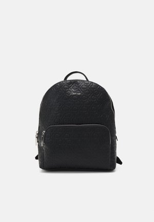 Sac à dos noir Calvin Klein avec motif de logo en relief, poche zippée à l'avant et poignée supérieure sur fond clair uni.