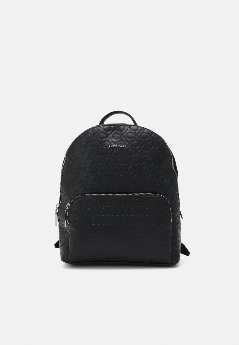 Sac à dos noir Calvin Klein avec motif de logo en relief, poche zippée à l'avant et poignée supérieure sur fond clair uni.