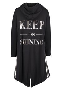 Vestido sudadera negro con el texto plateado "SIGUE BRILLANDO", mangas largas, rayas laterales y un dobladillo redondeado. Hecho de una tela suave.