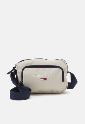 Beżowa nylonowa torba na ramię z granatowym zamkiem błyskawicznym i paskiem, posiada przednią kieszeń z logo "TOMMY JEANS" oraz drobny detal w postaci flagi z logo.