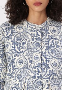 Veste à motif cachemire bleu marine et blanc avec col arrondi, fermeture boutonnée devant et poches latérales, confectionnée dans un tissu léger.