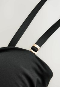 Sangle en tissu noir avec boucle métallique réglable ton or sur un vêtement noir sur fond clair.