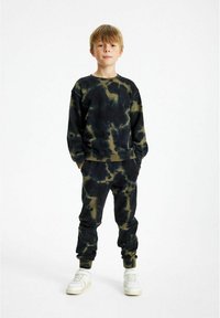 Set di felpa e pantaloni jogger tie-dye nero e verde oliva, materiale in cotone morbido, vestibilità rilassata, polsini a costine, schemi di colore coordinati, indossato con sneakers bianche.