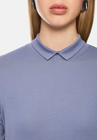 Helllila Polo-Shirt mit Kragen, glattem Material und dezenten Nähdetails. Keine sichtbaren Muster oder Verzierungen.