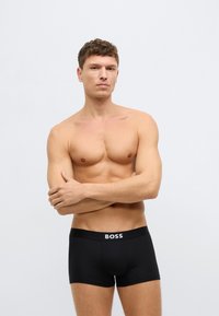 Czarne bokserki o dopasowanym kroju z elastycznym pasem w talii, na którym znajduje się biały napis "BOSS". Model prezentuje neutralną pozę.