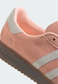 Világos rózsaszín velúr sneaker szürke részletekkel és texturált gumitalppal. Átfedő csíkokkal és párnázott szegéllyel a kényelem érdekében.