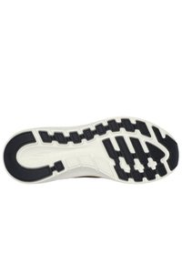 Suela de goma negra con patrones texturizados y surcos, que cuenta con una entresuela blanca y una ligera curva en el talón para mejorar la tracción.