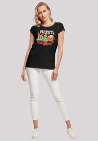 Zwarte katoenen T-shirt met een kleurrijke gedrukte afbeelding van kerstelementen en tekst. Gecombineerd met witte slim-fit broek en witte schoenen.