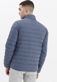 Viegls pūkains mētelis akmens zilā krāsā. Iespējas horizontāla quiltēšana un augsta apkakle. Gluda, ūdensizturīga auduma.