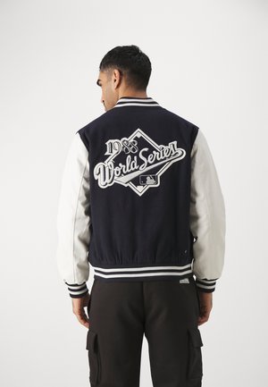 Cazadora varsity en azul marino y blanco con el logotipo bordado de "World Series 1988" en la parte posterior, puños y dobladillo a rayas, y textura de tela suave.