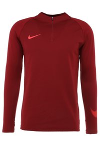 Chemise de sport rouge à manches longues avec col demi-fermeture éclair. Présente le logo Nike en orange vif et des accents texturés sur les manches. Finition en tissu lisse.