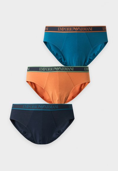Trois slips pour hommes Emporio Armani en bleu, orange et bleu marine foncé avec ceintures élastiques brandées sur fond uni.