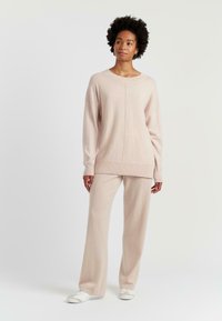 Pull en tricot rose clair avec des manches larges et un col rond, assorti à un pantalon ample. Texture douce et détails de couture subtils.