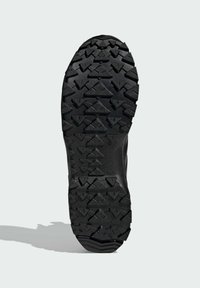 Black rubber shoe sole featuring a textured, multidirectional tread pattern with triangular and geometric shapes for traction.