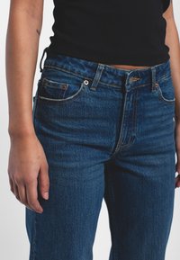 Dark blue denim jeans with a classic five-pocket design, featuring copper hardware and subtle stitching details. Slim fit, medium rise.