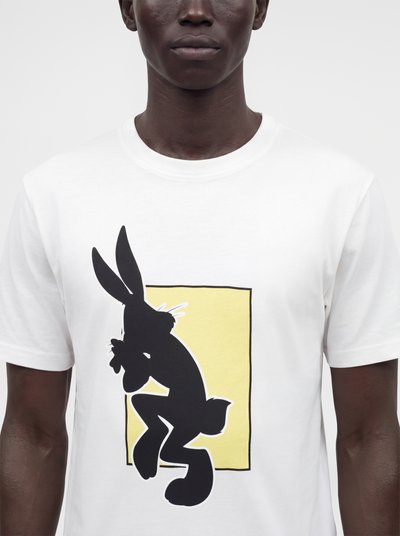 Homme portant un t-shirt blanc avec une silhouette noire de lapin sur un fond rectangulaire jaune à l'avant.