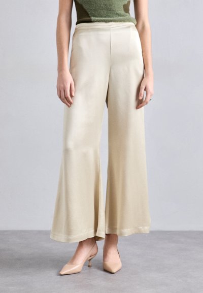 Beige Culotte-Hosen mit glatter, glänzender Textur und hoher Taille, kombiniert mit hautfarbenen High Heels.