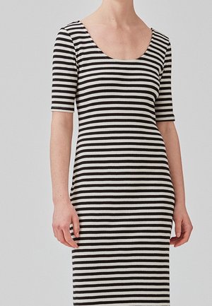 Femme portant une robe ajustée côtelée avec des rayures horizontales noires et blanches et des manches aux coudes.