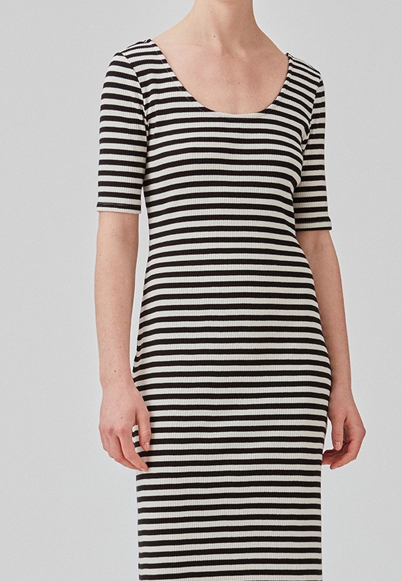 Femme portant une robe ajustée côtelée avec des rayures horizontales noires et blanches et des manches aux coudes.