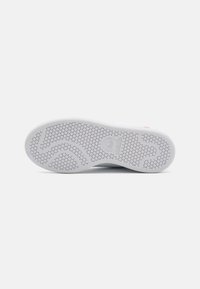 Vit idrottssko sula med ett strukturerat hexagonalt mönster, som har en framträdande adidas-logotyp och en slät, rundad form.