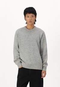 Gai pelēks adīts džemperis ar apaļu kakla izgriezumu, ribotām piedurknēm un apakšmalu. Iezīmēts ar teksturētu rakstu un brīvu piegriezumu. Kombinēts ar melniem bikšiem.