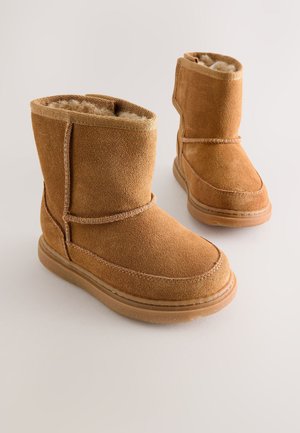 Brūnas zamšādas potīšu zābaki ar mīkstu kažokādu oderējumu, apaļu purngalu, šūtas detaļas un gumijas zolēm. Dizainā ir salokāms augšdaļas elements.