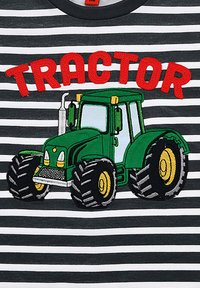 Grau-weiße gestreifte T-Shirt mit einem gestickten grünen Traktor mit gelben Akzenten und großen schwarzen Reifen, über dem Text "TRACTOR" in Rot.