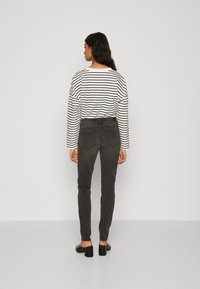 Čierne skinny džínsy s stredne vysokým pásom, skombinované s dlhým rukávom bielou a čiernou pruhovanou košeľou, so zobrazením rovného pohľadu zozadu.