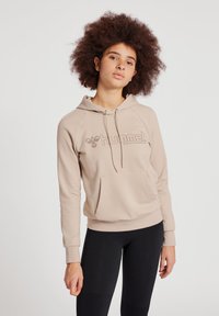 Hoodie beige avec une poche avant, des cordons de serrage ajustables et des manches raglan. Présente un logo ton sur ton sur la poitrine et une texture douce.