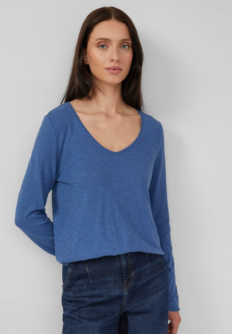 Maglia blu a maniche lunghe con scollatura a V, realizzata in tessuto testurizzato. Abbinata a pantaloni in denim scuri, caratterizzati da una vestibilità rilassata e da un design semplice.