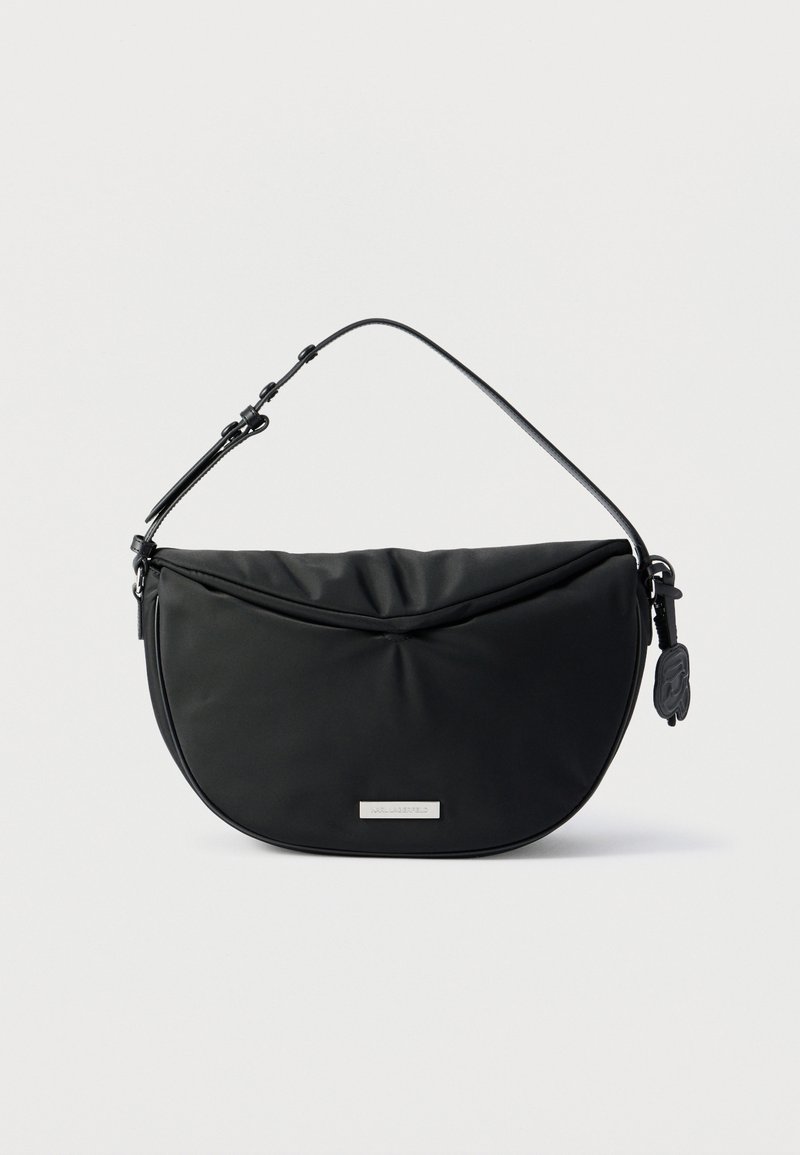 Μαύρη τσάντα ώμου σε σχήμα ημισελήνου με ρυθμιζόμενο λουράκι και μικρή μεταλλική πλακέτα με λογότυπο στο μπροστινό μέρος, πάνω σε ανοιχτόχρωμο φόντο.