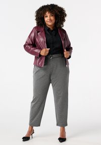 Bordeaux leren motorjack over een zwart gestreept overhemd, gecombineerd met hoge, grijze geblokte broek en zwarte pumps met een spitse neus.