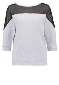 Lichtgrijze trui met een zwart doorschijnend paneel over de schouders. Heeft een ontspannen pasvorm, lange mouwen en een ronde halslijn.