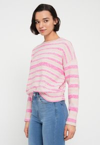 Ανοιχτό ροζ πουλόβερ με οριζόντιες φωτεινές ροζ ρίγες, στρογγυλή λαιμόκοψη και μακριά μανίκια, σε συνδυασμό με ψηλόμεσα μπλε τζιν. Μαλακή υφή.