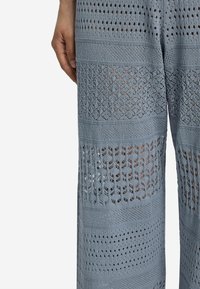 Ljust blå virkade byxor med en blandning av öppna mönster och fasta sektioner, med vida ben och en strukturerad, andningsbar design.