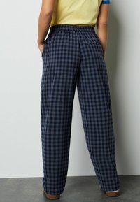 Marineblauwe en grijze geruite broek gemaakt van lichtgewicht stof. Voorzien van een elastische tailleband en zijzakken. Rechte pijpen.