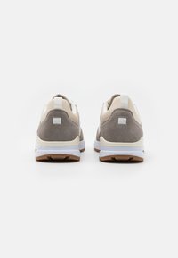 Sneakers con tomaia in pelle beige e accenti in suede grigio. Suole in gomma bianca con superficie testurizzata e un'etichetta sul tallone per una facile calzata.