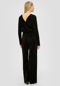 Zwarte jumpsuit met lange mouwen en een diepe V-rug. Kenmerkt zich door verticale geribbelde textuur en een ruime benen ontwerp. Glad materiaal met een subtiele glans.