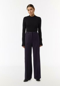 Black fitted turtleneck sweater paired with high-waisted, wide-leg dark purple trousers. Smooth texture and subtle detailing on sleeves.