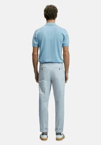 Helles blaues Kurzarm-Polohemd, kombiniert mit hellgrauen Hosen mit Gesäßtaschen und goldenen Akzenten, getragen mit grauen und braunen Sneakers.