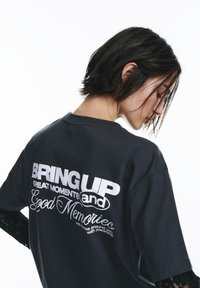 Črna bombažna majica z belim napisom na hrbtni strani, ki pravi "BRING UP GREAT MOMENTS and Good Memories" v različnih pisavah, z okroglim izrezom.