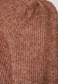 Gros plan sur un tissu tricoté doux et épais avec un motif moucheté marron et blanc, doté d'une texture côtelée.