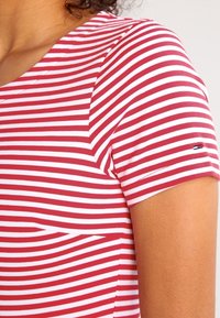 Röd och vit randig t-shirt, korta ärmar, rundad halsringning, mjuk bomullsblandning, har en liten logotyp nära ärmen och en ficka med lapp.