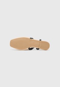 Sandale negre cu talpă plată, având două curele subțiri și o talpă din cauciuc texturat, de culoare bej. Linii curate și design minimalist.