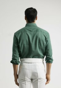 Camisa verde de manga larga con mangas remangadas, detalle en la parte trasera, combinada con pantalones blancos de talle alto que tienen bolsillos laterales y traseros.