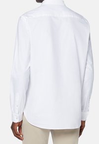 Bakifrån vy av en man klädd i en långärmad vit skjorta med knäppta manschetter, i kombination med ljusa byxor. Enkel, klassisk stil.