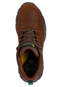 Bota impermeable de cuero marrón con cordones verdes y marrones, cuello acolchado y suela de goma negra texturizada. Presenta un forro amarillo y una marca.